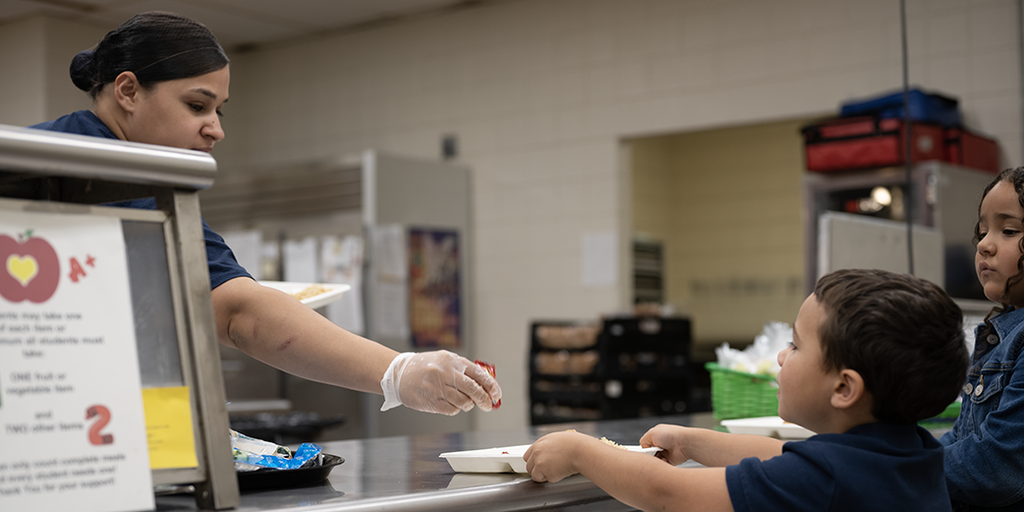 Cafeteria employee serving students in tray line