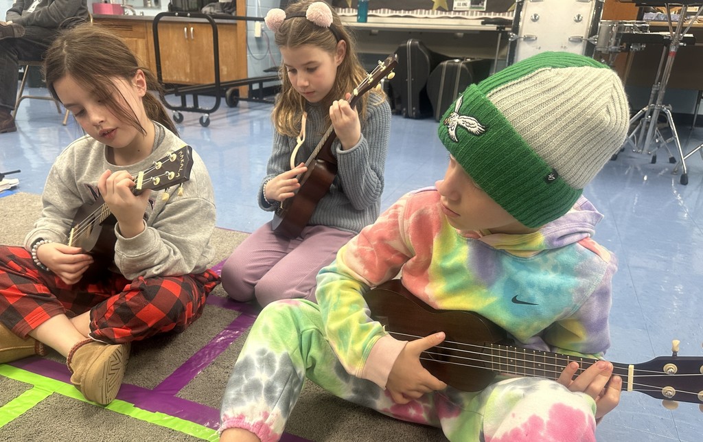 three third grade students strumming ukuleles