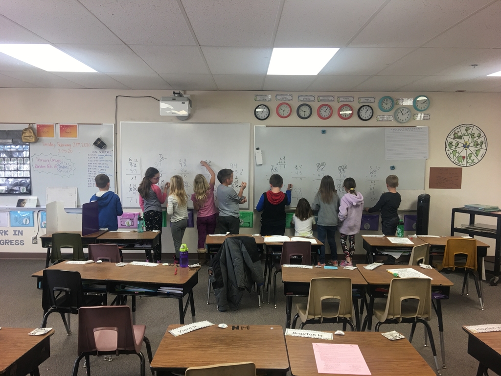 Eight second graders practice math problems together at the whiteboard. 