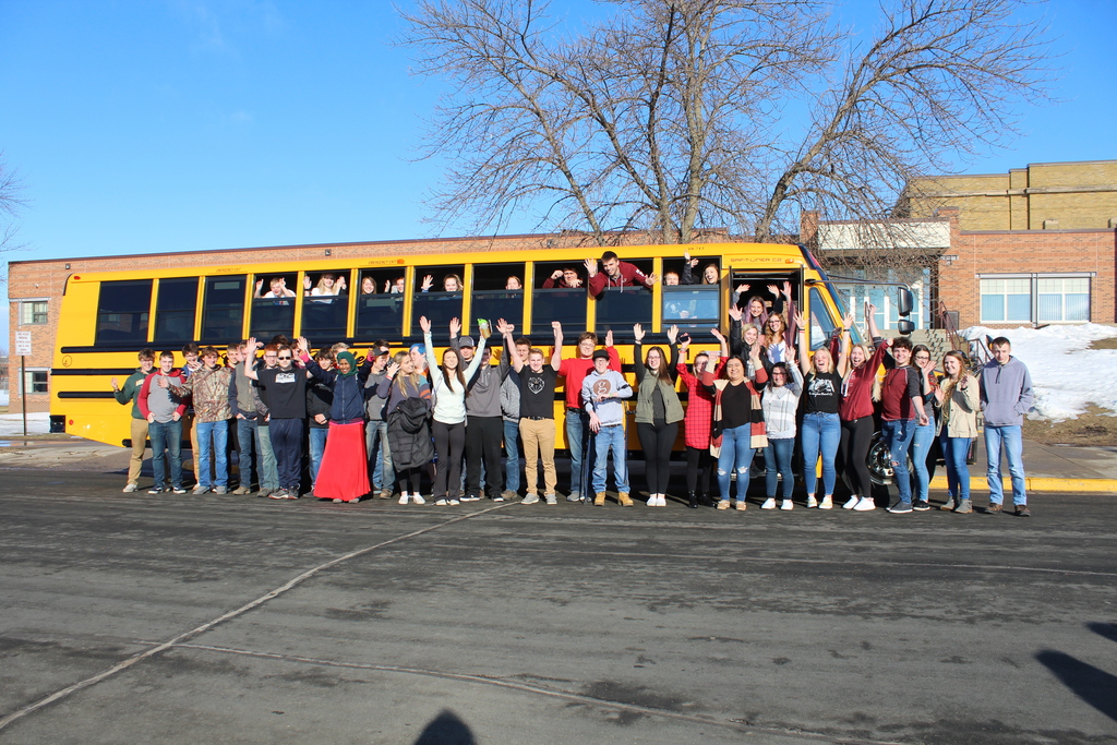 senior students arms up in front of bus