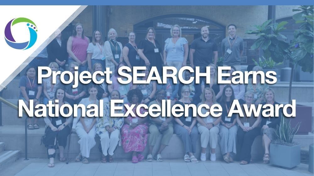 A group shot of men and woman in front of a building with a blue opaque overlay that say the words "Project SEARCH Earns National Excellence Award". 