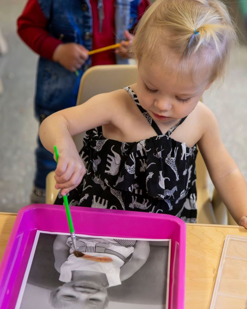 Little girl painting over a black and white photo of herself.