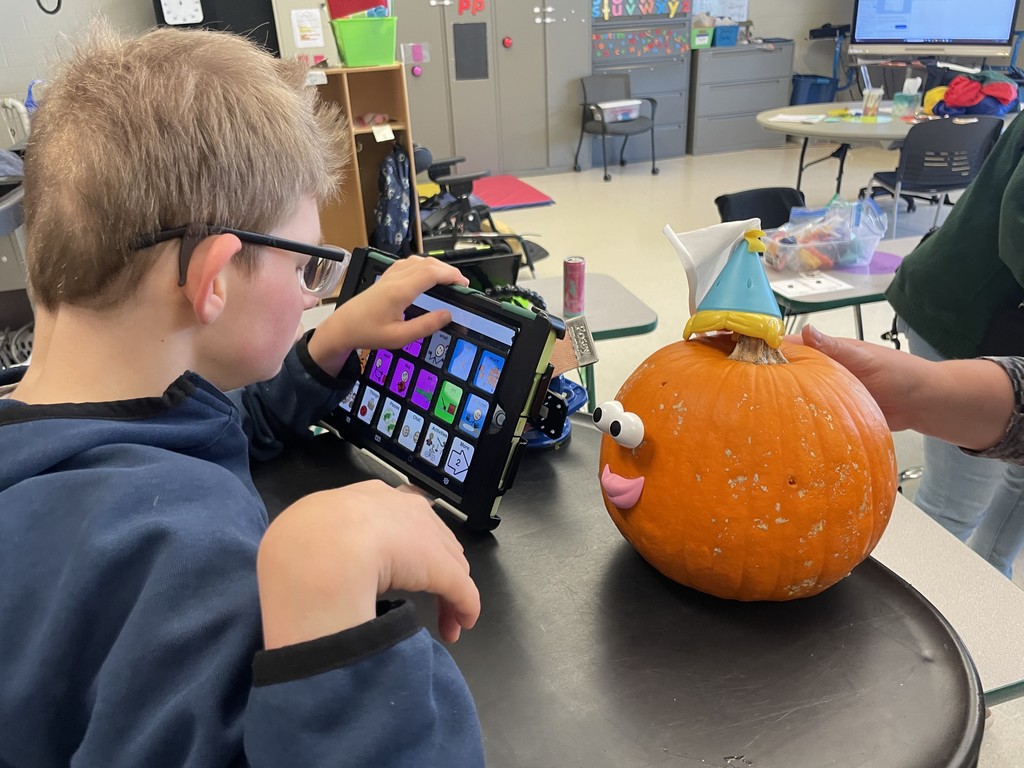Student using communication device and building a pumpkin with potato head pieces. 