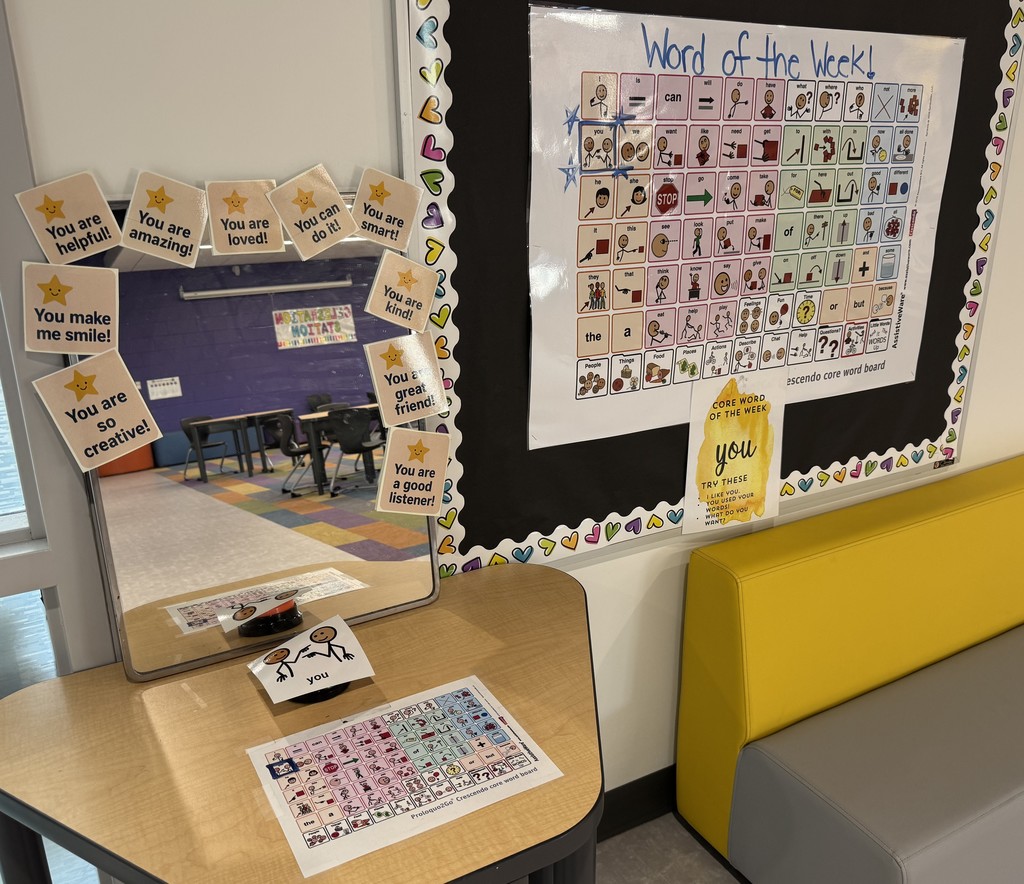 A hallway communication station featuring an AAC Core Word of the Week bulletin board and a mirror surrounded by positive affirmation cards for the core word "YOU".