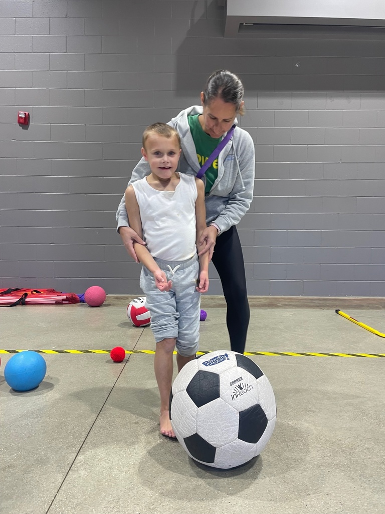 PE Teacher helping student kick the ball.