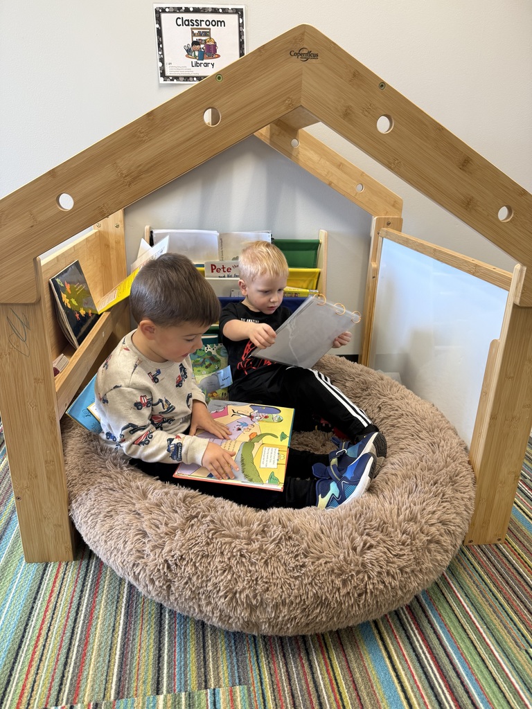 Two young children sit in a cozy reading nook looking at books.