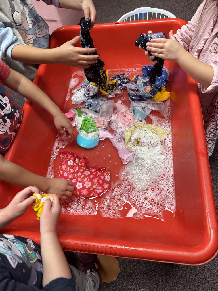 Children washing small clothes in a soapy water bin.