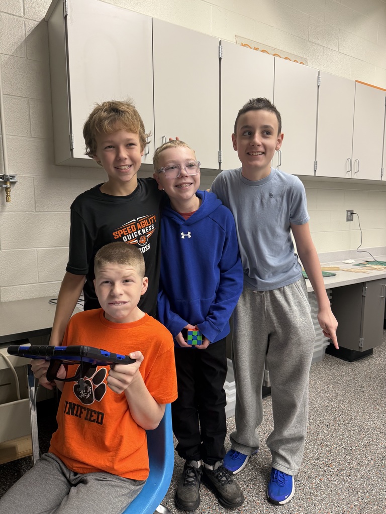 Four students standing around each other and smiling. One student is holding a tablet. 