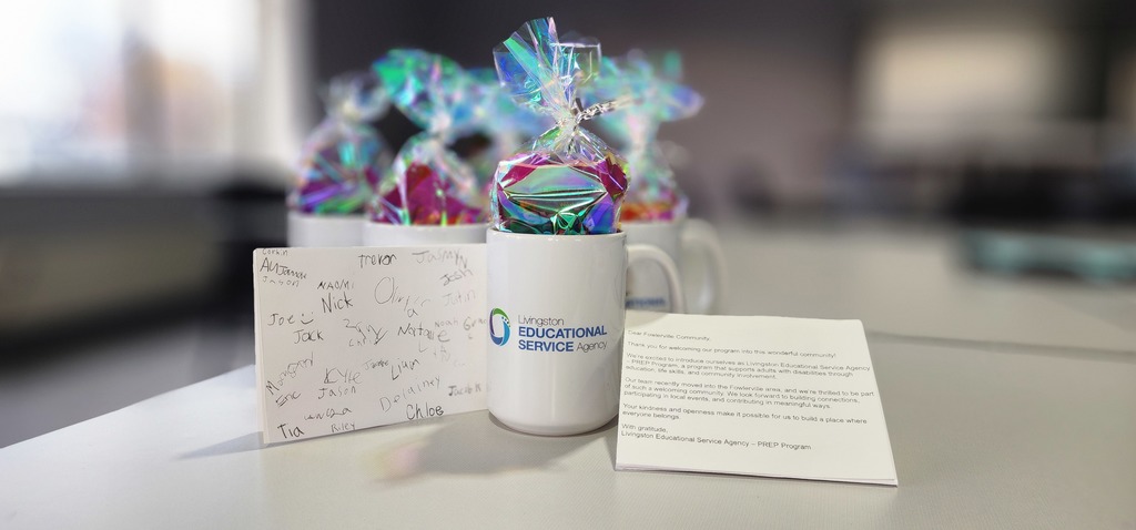 Coffee mugs filled with goodies, sitting on a table with one focused mug in the middle. The focused mug has a card sitting on each side.