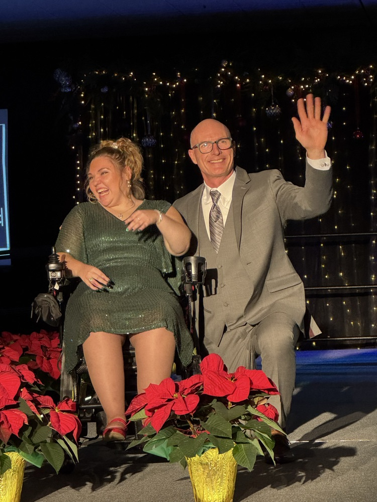 Two people on stage, one kneeling and one in a wheelchair