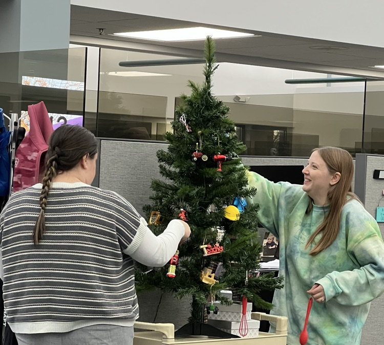 Two women decorate a small tree for Christmas.