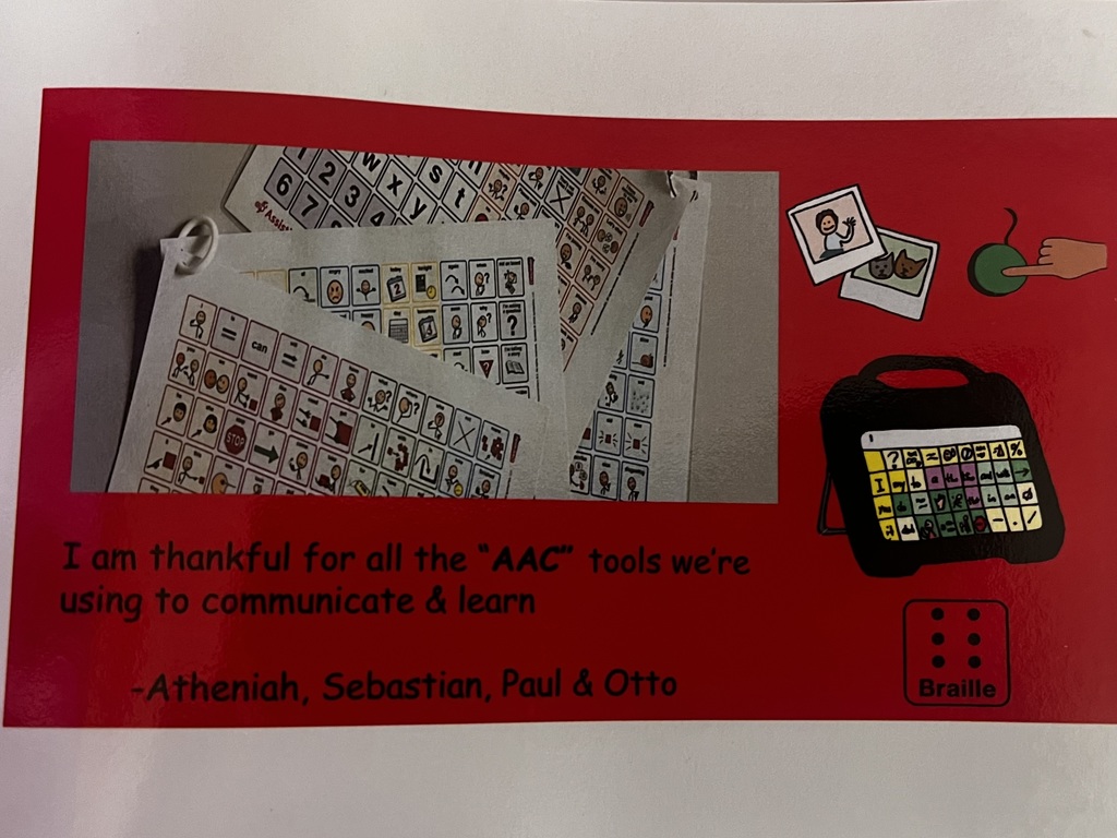 AAC boards, pictures, a switch, and a braille symbol on a red piece of construction paper that reads "I am thankful for all the AAC tools we're using to communicate and learn, signed Atheniah, Sebastian, Paul, & Otto.