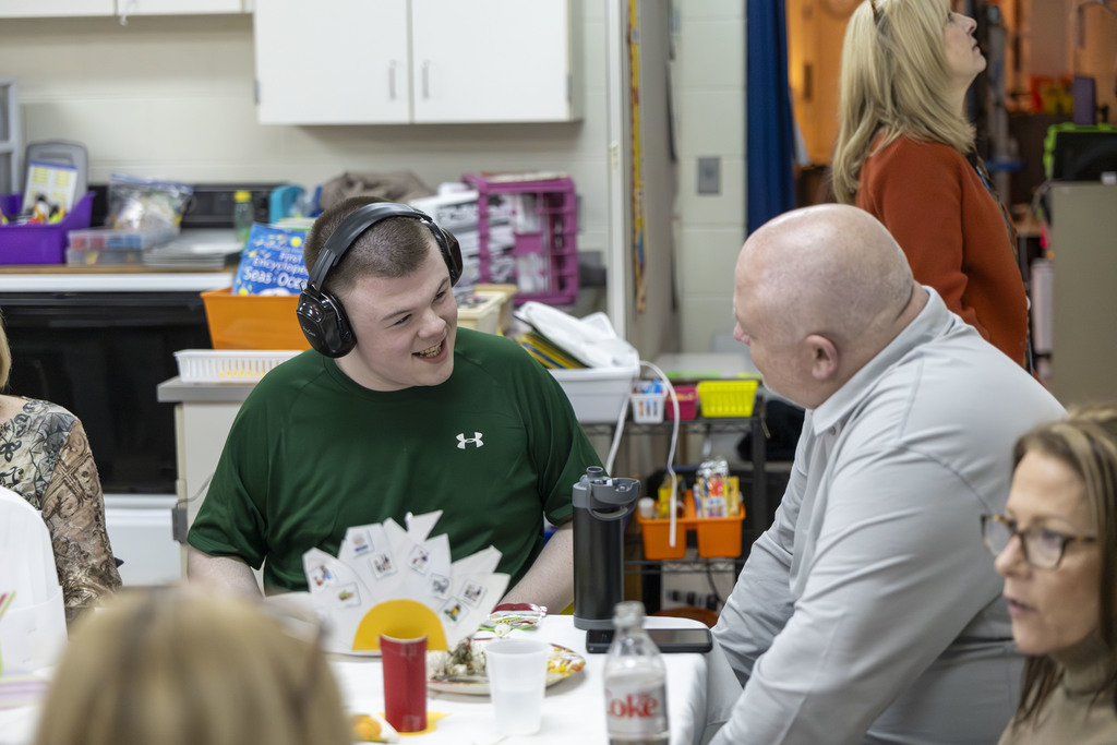 Student with headphones on smiling and talking to an adult.