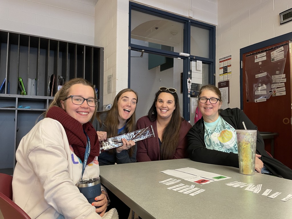 Four staff sitting at table  smiling with candy bar in hands.