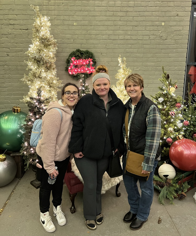 Three women stand in front of Christmas display. 