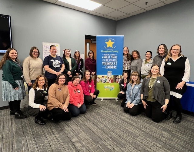 A group of people posing around a sign for the Great Start Collaborative. 