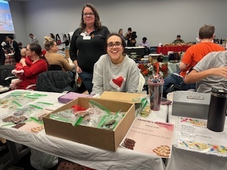 1 women siting and 1 standing behind her at craft show table selling items