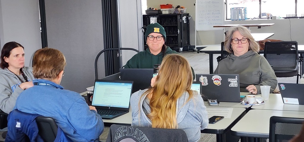 Five ladies sitting around a desk working on their laptops.