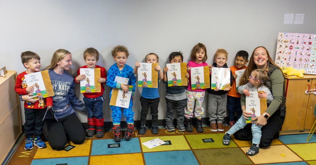 Group of kids and two teachers posing with books.