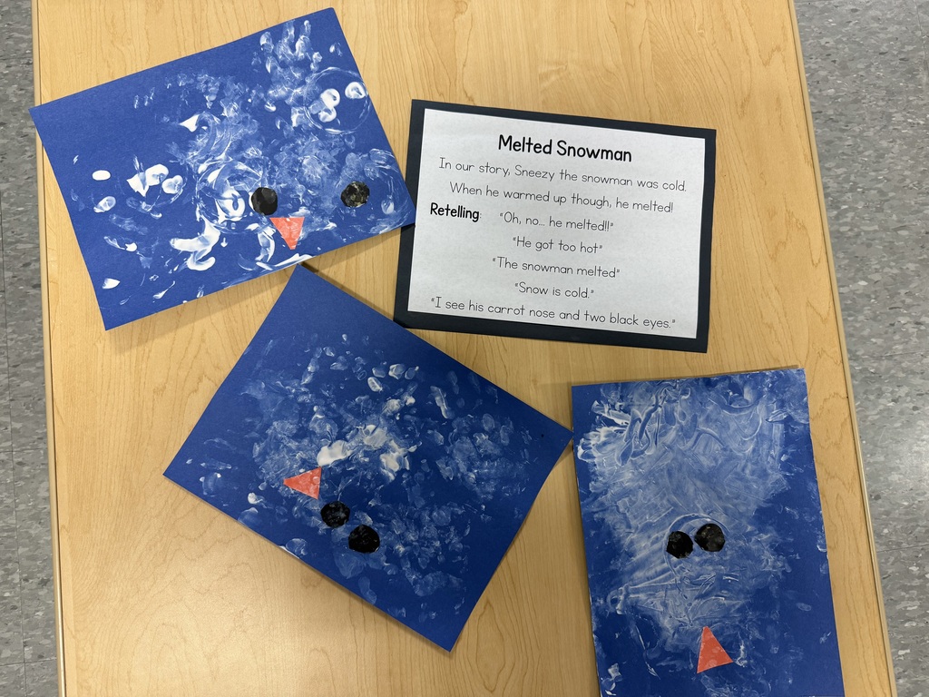 Children’s melted snowman art made with white paint on blue paper, with black eyes and orange carrot noses.