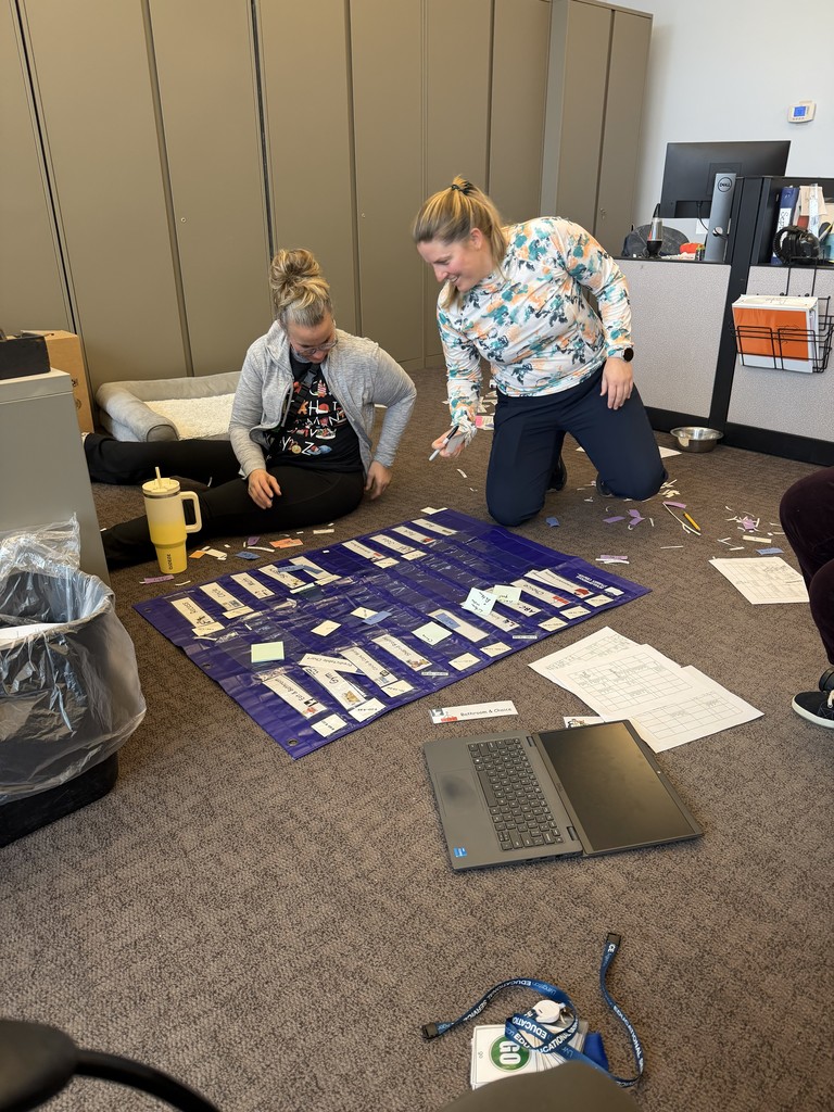 Two staff kneeling  over a pocket chart on the floor.