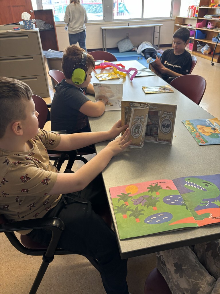 Three boys sitting around table reading books.