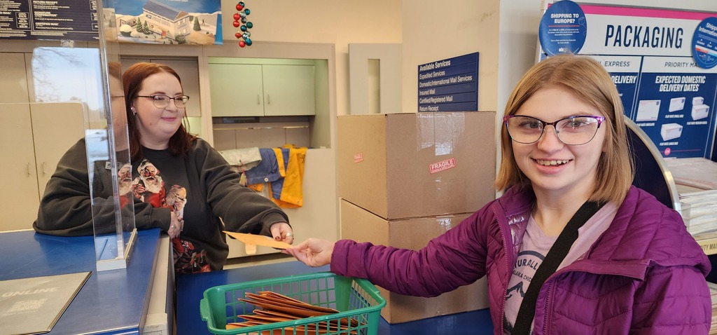 A young adult passing an envelope over the counter to a post person.