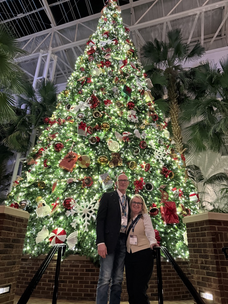 A happy couple standing in front of a brightly lit and decorated holiday tree.