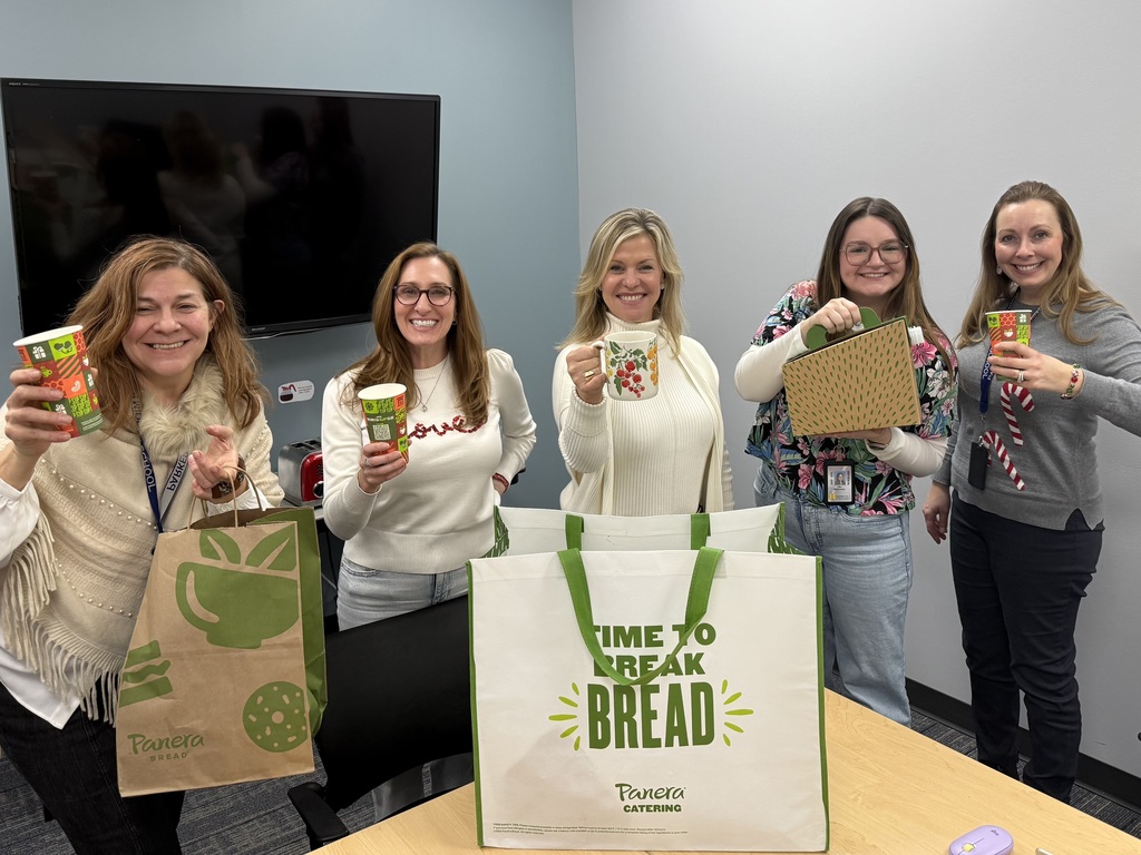 A group of woman holding up their coffee cups, smiling in front of a Panera Bread to-go bag.