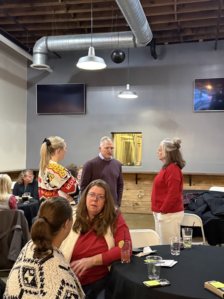Group of people 3  standing 2 sitting at a table 