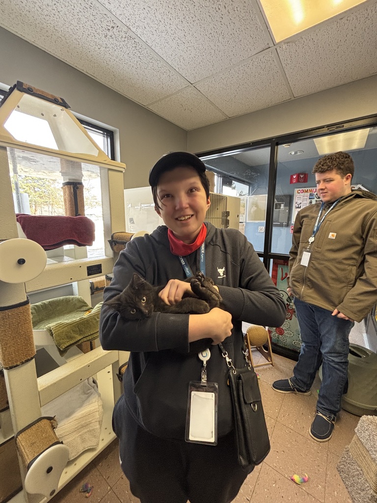 A female adult learner holding a cat , with a male learner standing in the background.