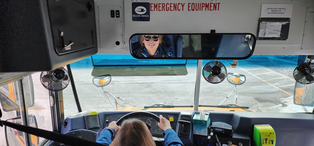 A female bus driver looking into the rear view mirror.