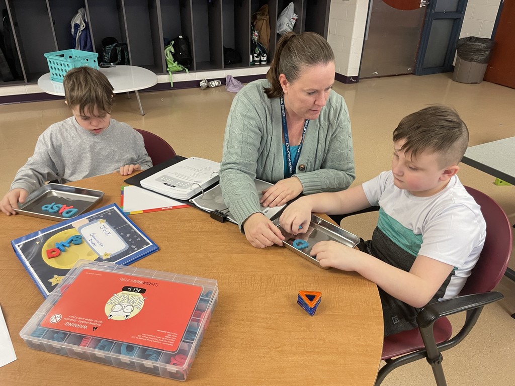 Teacher sitting between two students working with magnetic boards and letters.