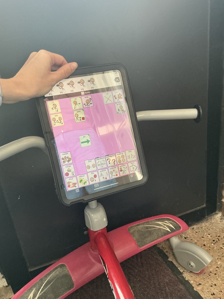 A small child's tricycle wiggle bike with someone holding a communication device up between the handlebars. 