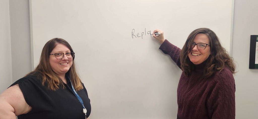 Two woman smiling in front of a white board.