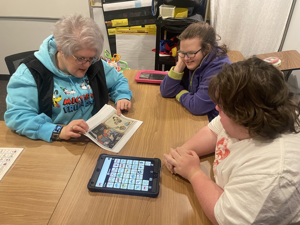 Teacher reading a page of a book to two students.