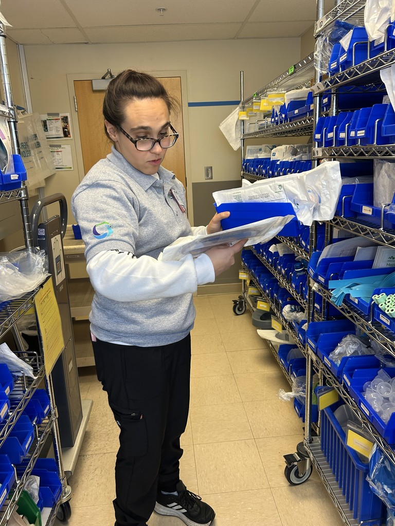 Woman in a room with blue bins on shelves stocking medical supplies