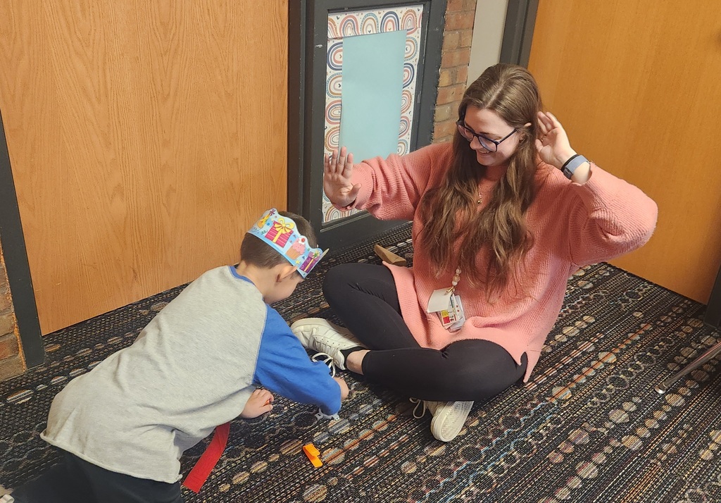 Adult woman sitting on the ground playing with a young boy.