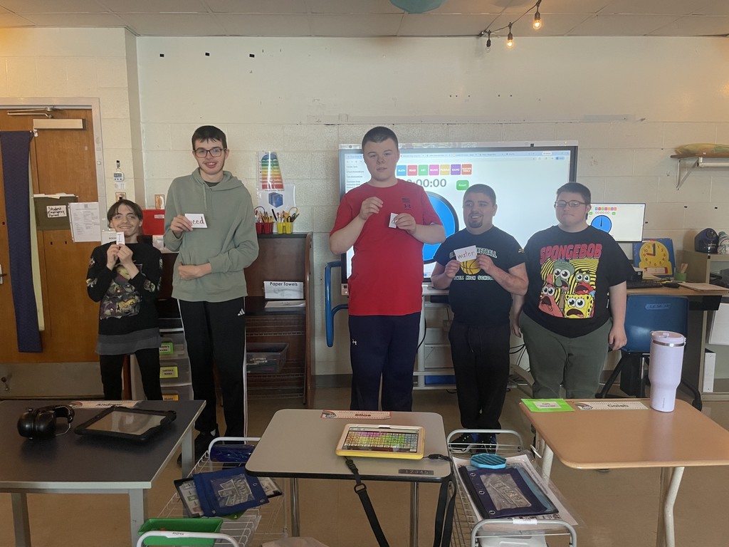 Five boys standing in the front of a classroom, holding a word in their hands.