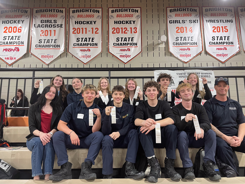 several students sitting on the bleachers holding white, championship ribbons. 