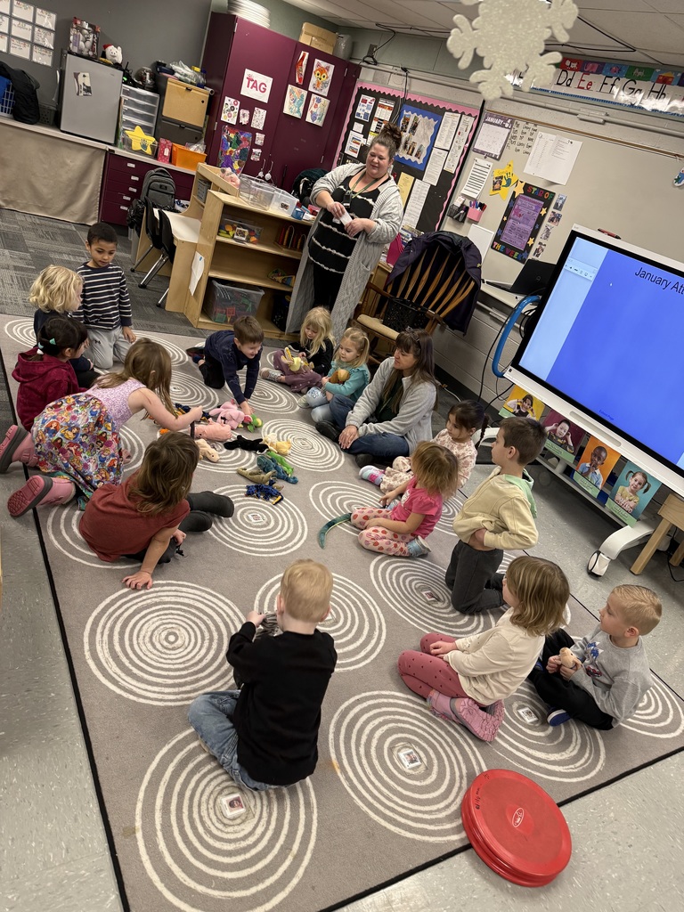 Preschool children sit in a circle on a rug, selecting stuffed animals as classroom pets.
