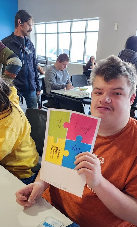 A young man holding up a project with four colorful puzzle pieces on construction paper.