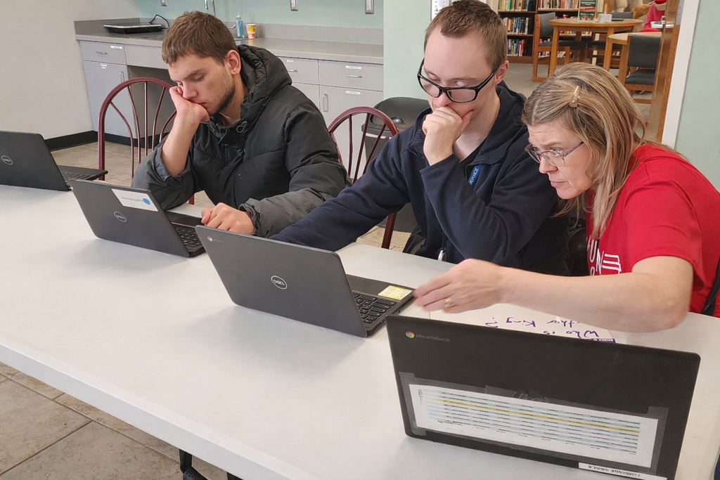 Two young men and a female sitting at a table, working on their laptops.