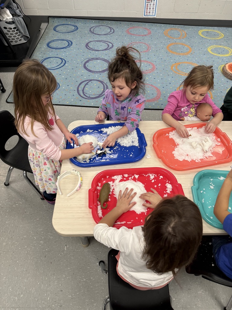 Preschool children explore artificial snow at tables, playing with winter animals and vehicles during a hands-on sensory activity.