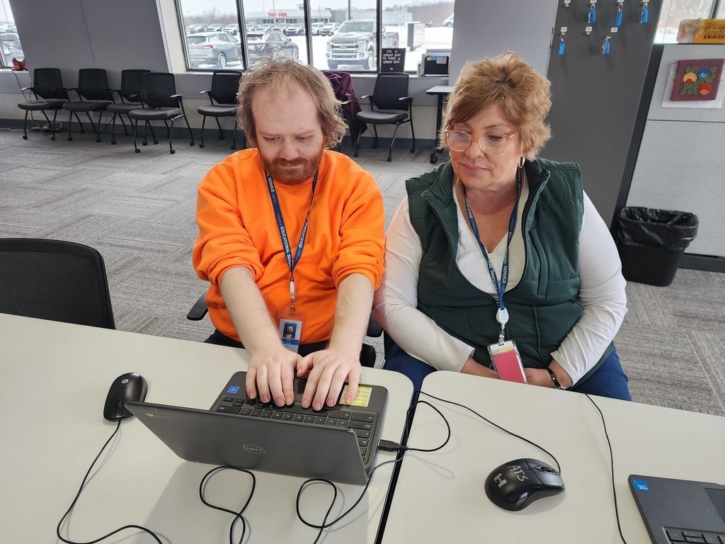 Young adult typing while a teacher watches on.