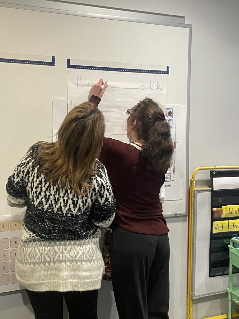 Student writing on the board , supported by a staff member.
