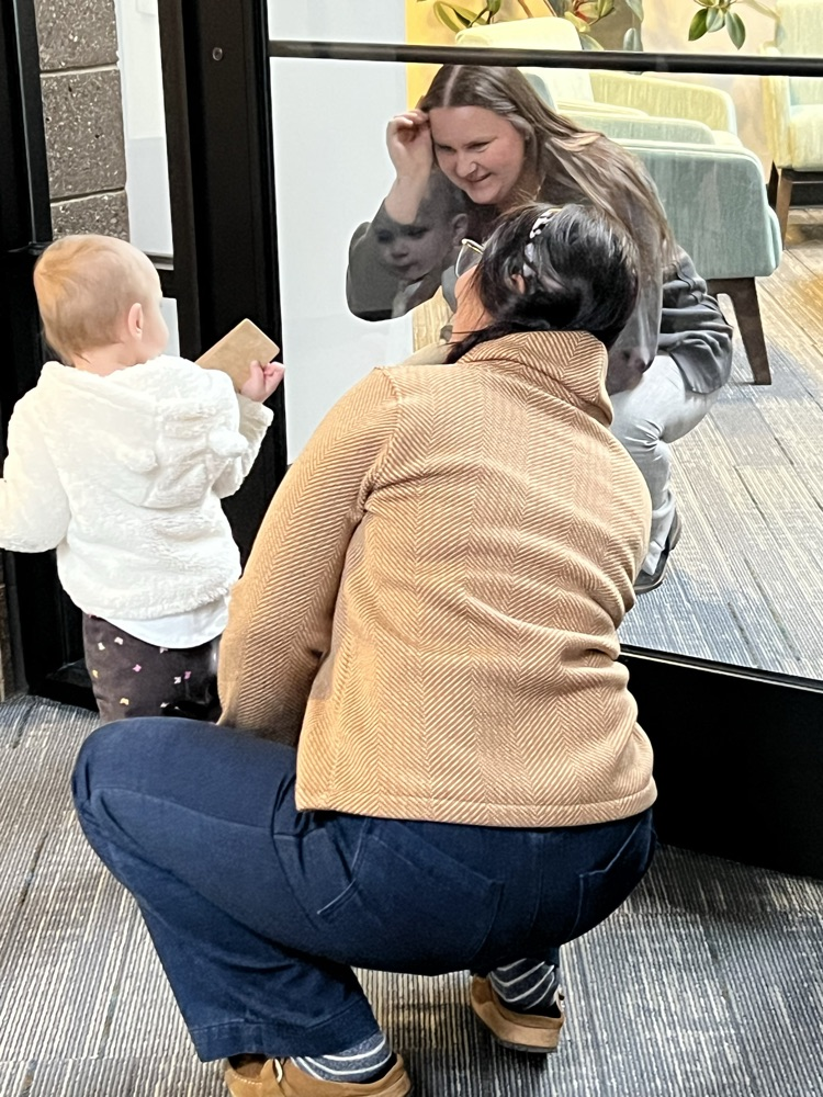 Two staff members playing peek a boo with young child.  