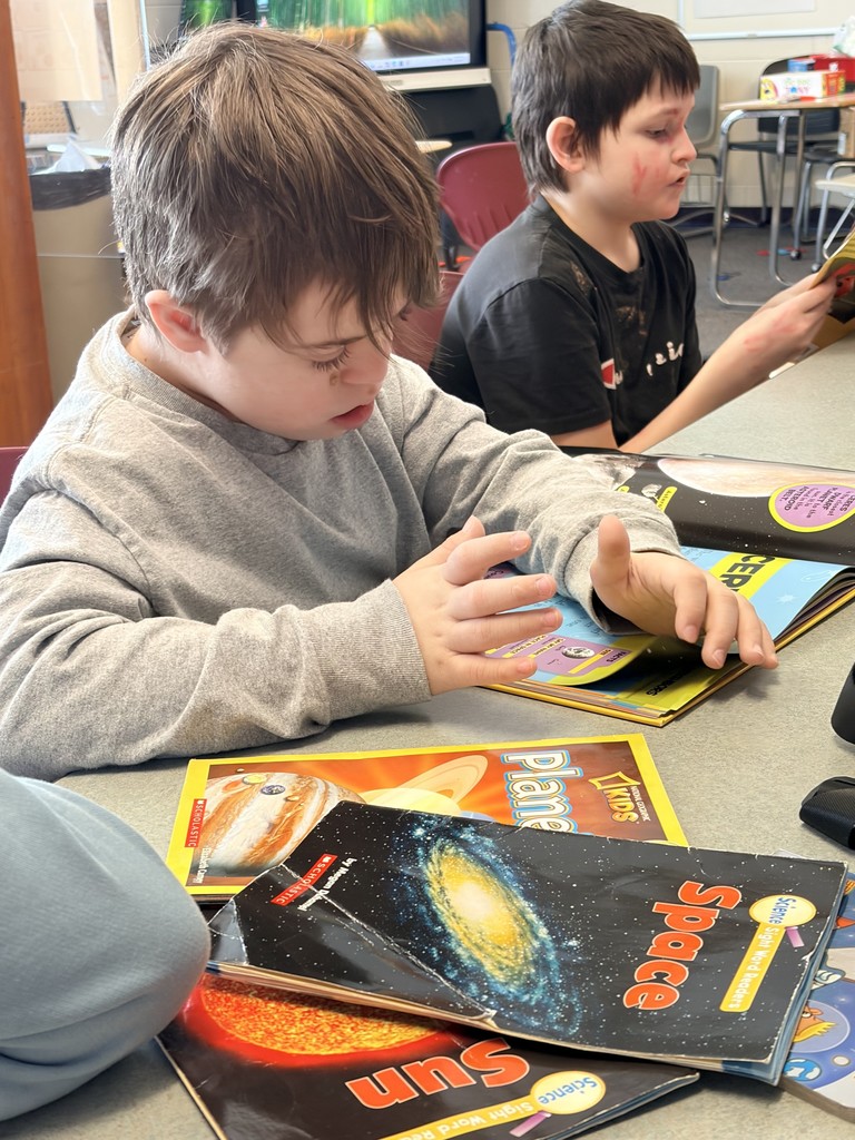 Boy looking at books about space, sitting at a table.