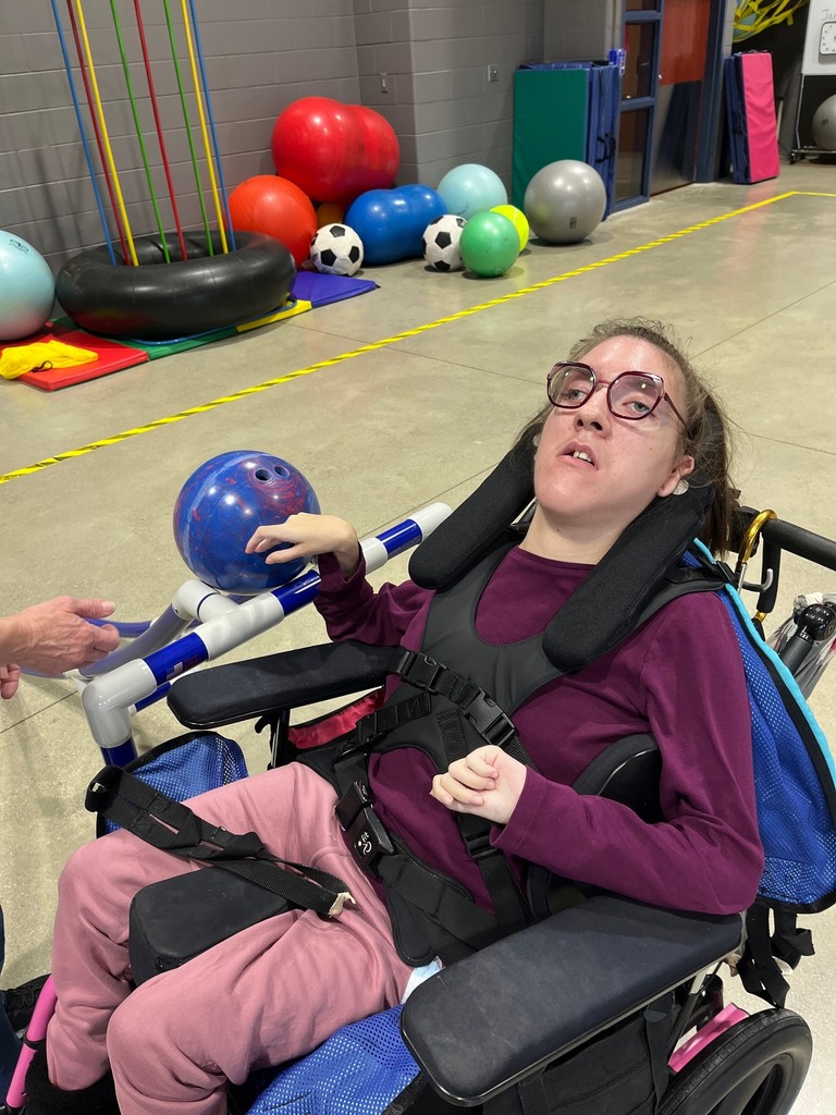 Young women who uses a wheelchair is pushing a bowling ball down a ramp.