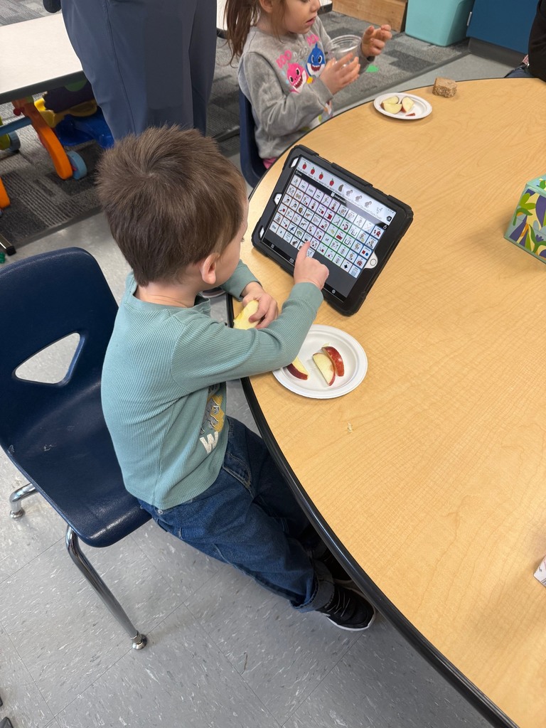 A student uses a core communication board at the breakfast table to identify the fruit he is eating.